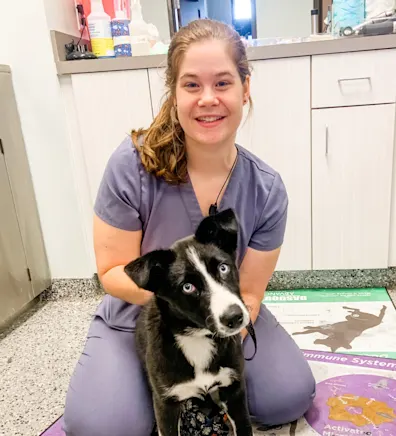 Alice Parker smiling kneeling down next to a black and white dog Alice Parker smiling kneeling down next to a black and white dog