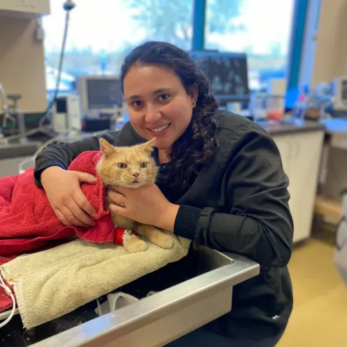 Woman smiling while holding an orange cat wrapped in a red towel.