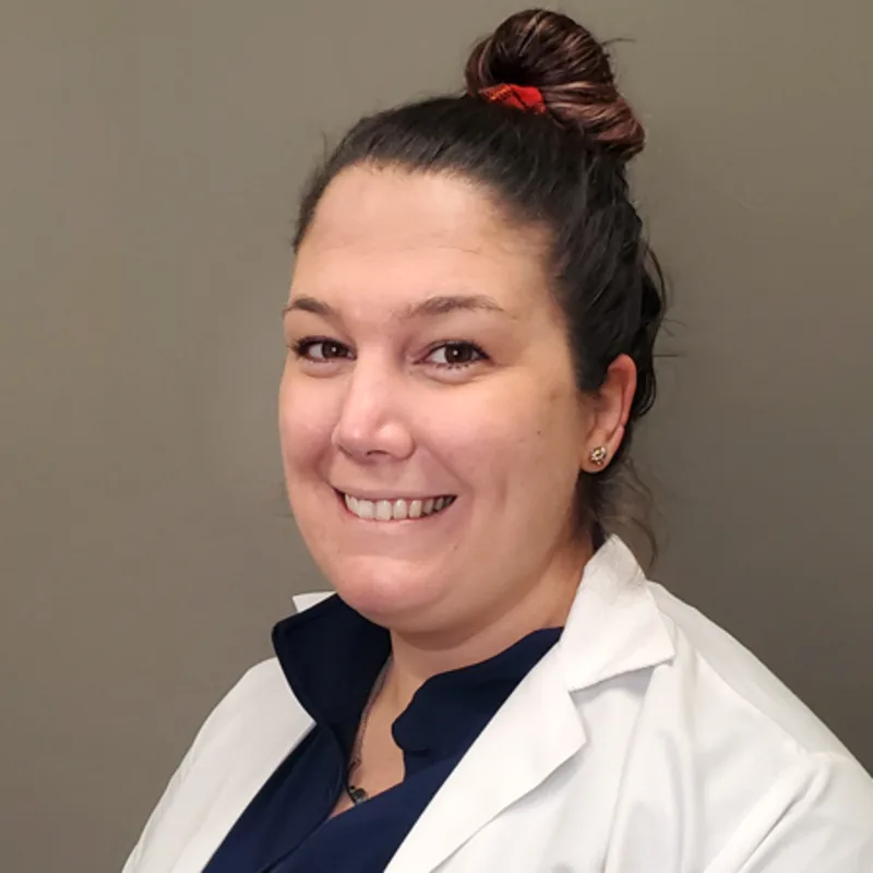 Jamie Wojtkiewicz smiling standing in front of a tan wall wearing a white lab coat Jamie Wojtkiewicz smiling standing in front of a tan wall wearing a white lab coat