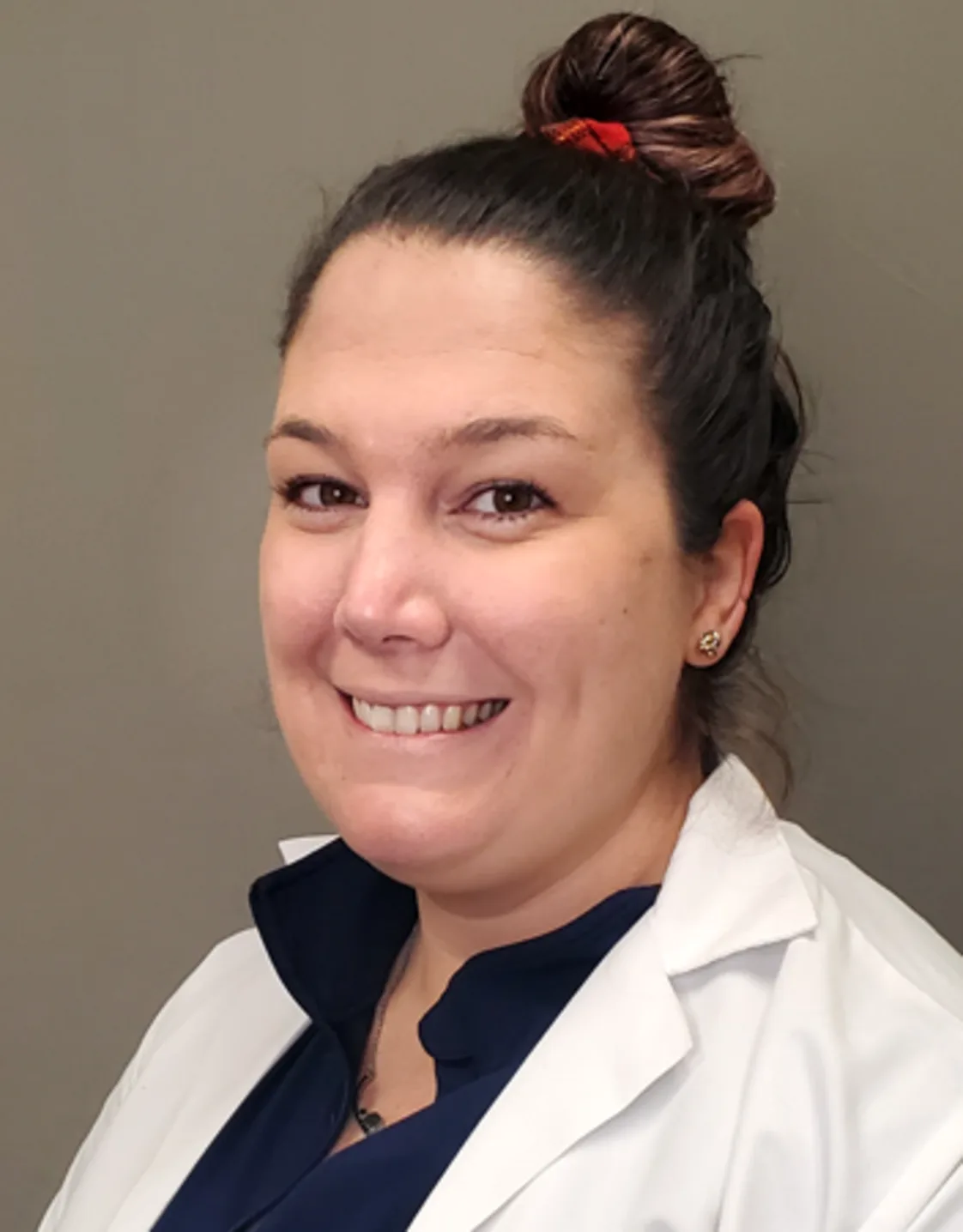 Jamie Wojtkiewicz smiling standing in front of a tan wall wearing a white lab coat Jamie Wojtkiewicz smiling standing in front of a tan wall wearing a white lab coat