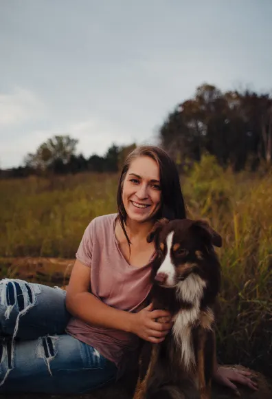 Woman sitting with her dog in a field and smiling at the camera.