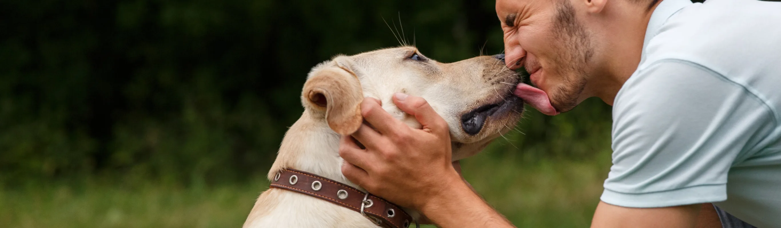 a man bends down while getting licked on the mouth by a dog