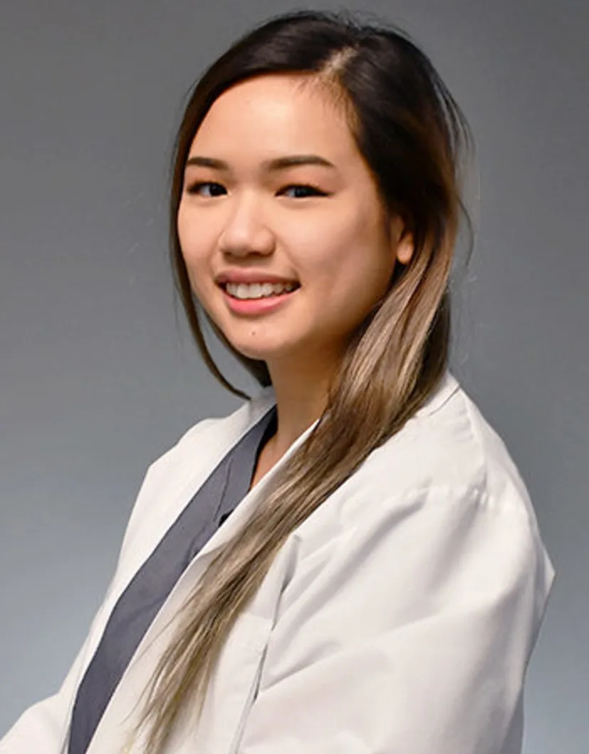 Kathy Vu smiling standing in front of a grey wall wearing a white lab coat