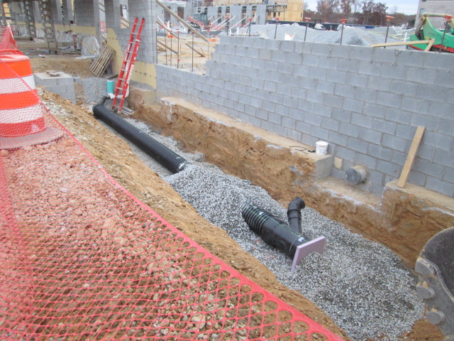 A view of the foundation of VVC Short Pump showing gravel, a grey wall, and a pipe