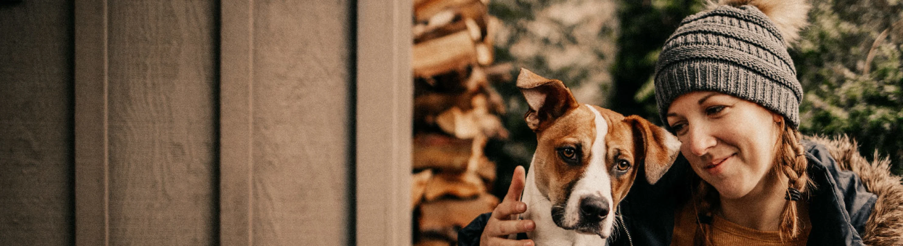 A dog snuggling with its owner outdoors next to a stack of firewood