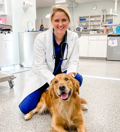 Dr. Anna Decker smiling kneeling down next to a Golden Retriever laying on the floor Dr. Anna Decker smiling kneeling down next to a Golden Retriever laying on the floor