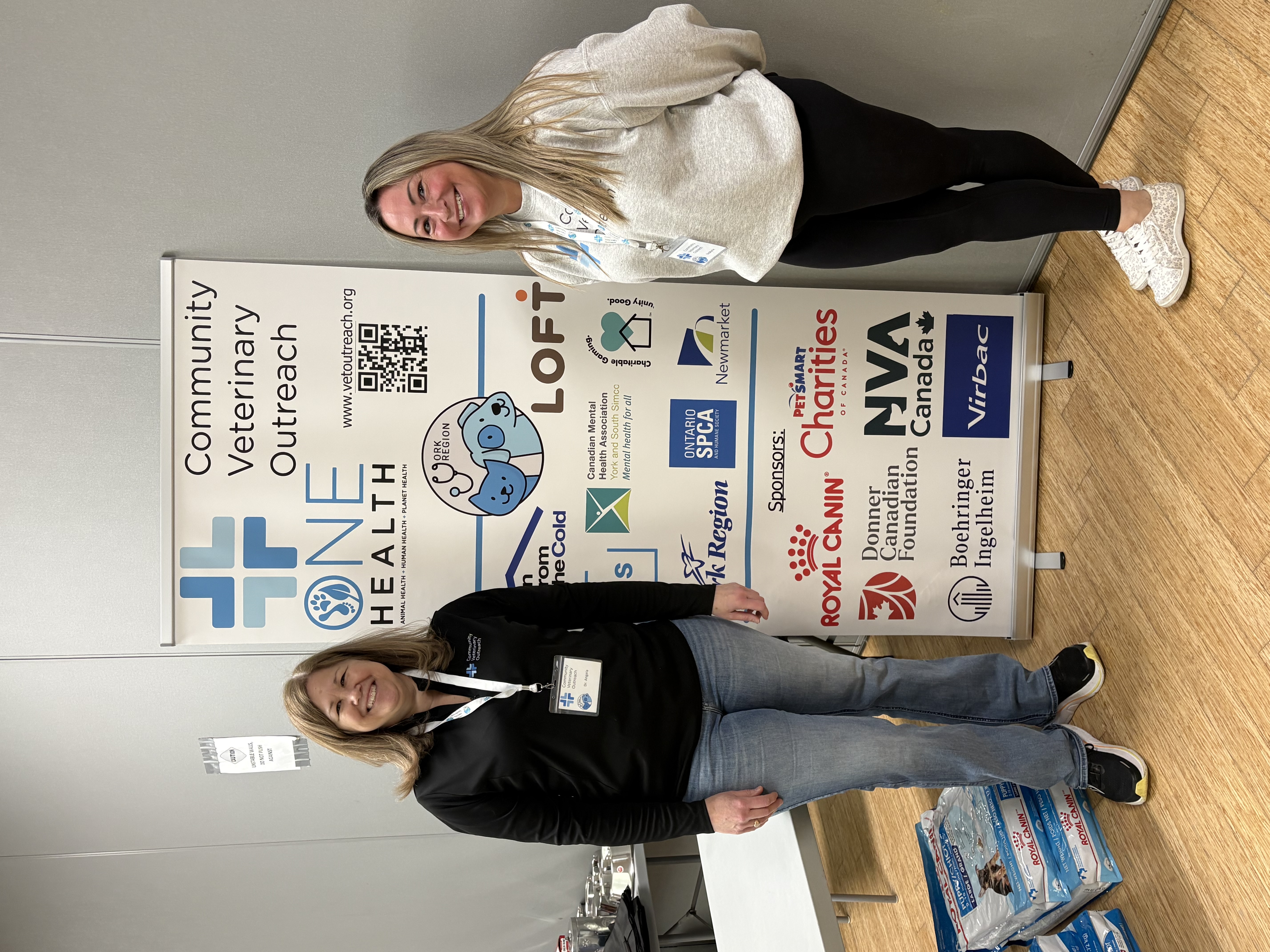 Two team members in front of the community veterinary outreach banner