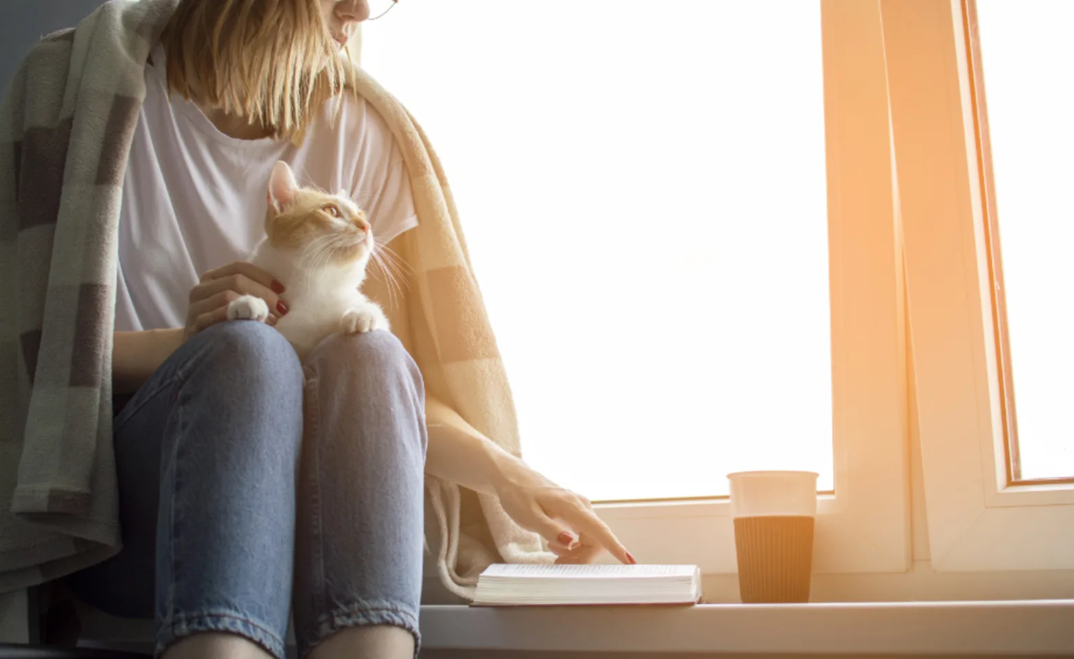 Girl reading with cat in her lap a blanket around her