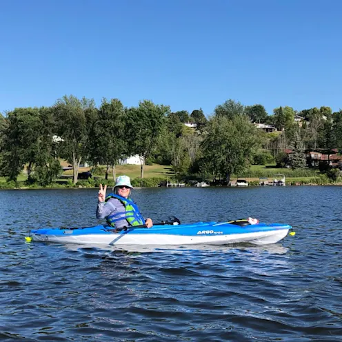 Sandra McBride smiling with hand in peace sign sitting in a kayak on a lake. Sandra McBride smiling with hand in peace sign sitting in a kayak on a lake.