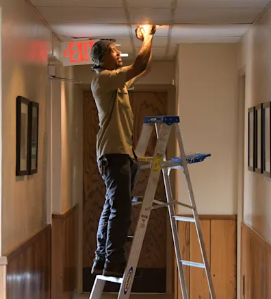 Tony standing on a ladder and fixing a lightbulb