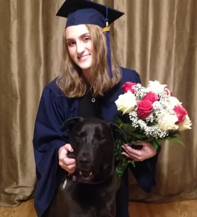 Staff photo of Lianne in a cap and gown, holding flowers with a dog in front of her Staff photo of Lianne in a cap and gown, holding flowers with a dog in front of her