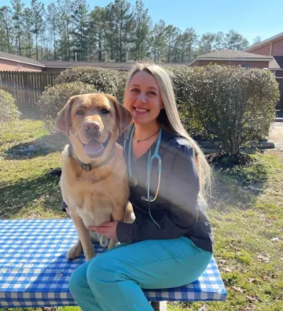 Morgan Bischoff sitting on an outside table with a dog. Morgan Bischoff sitting on an outside table with a dog.