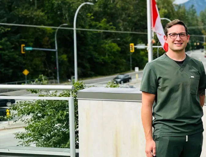 Dr. Harry Cozens smiling standing outside wearing green scrubs