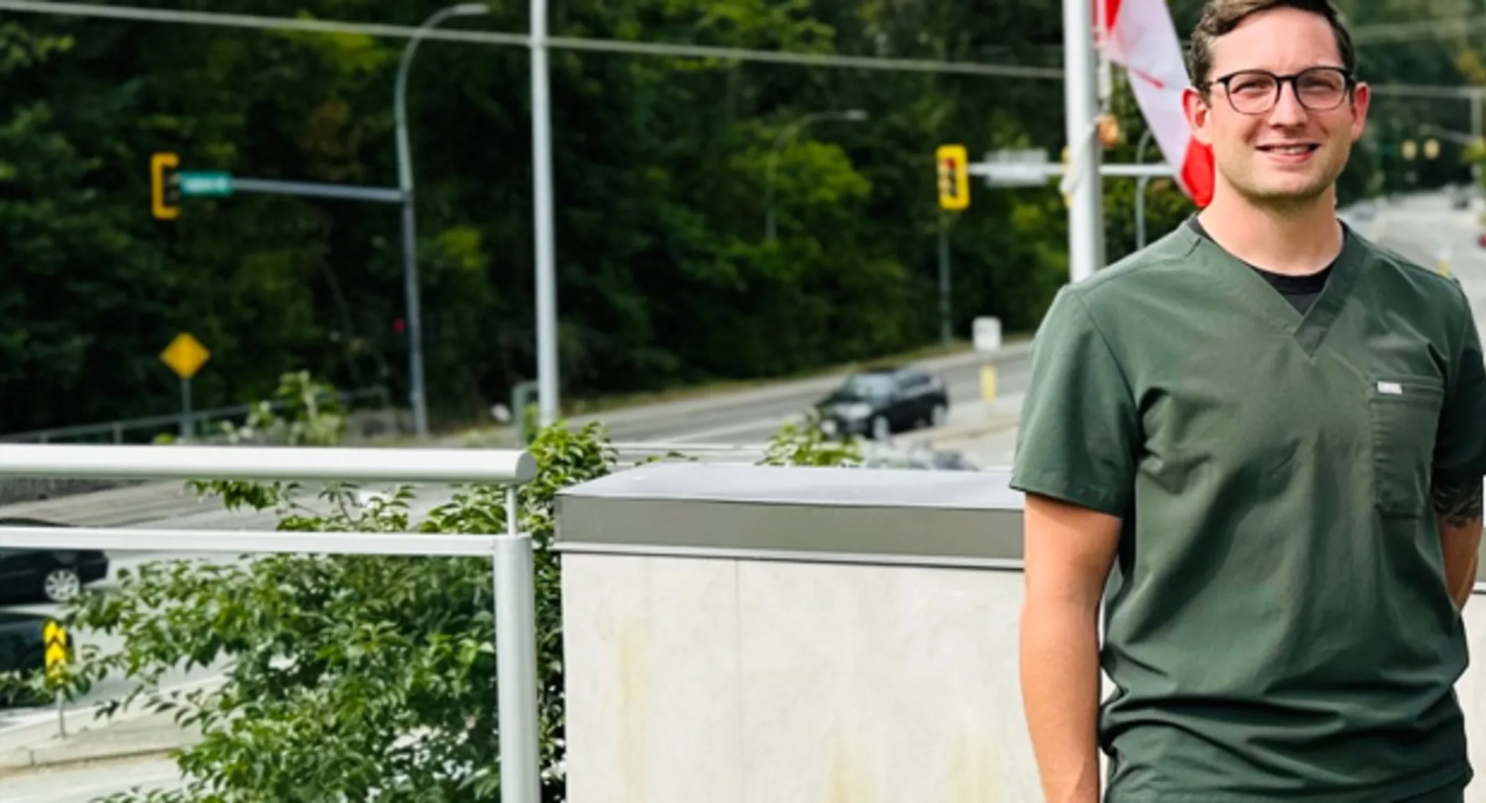 Dr. Harry Cozens smiling standing outside wearing green scrubs