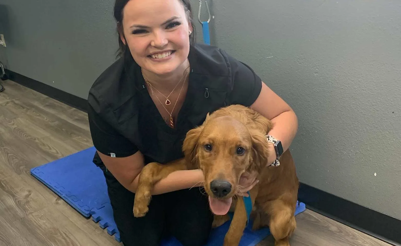 Staff in black scrubs smiling alongside a medium-sized brown dog.