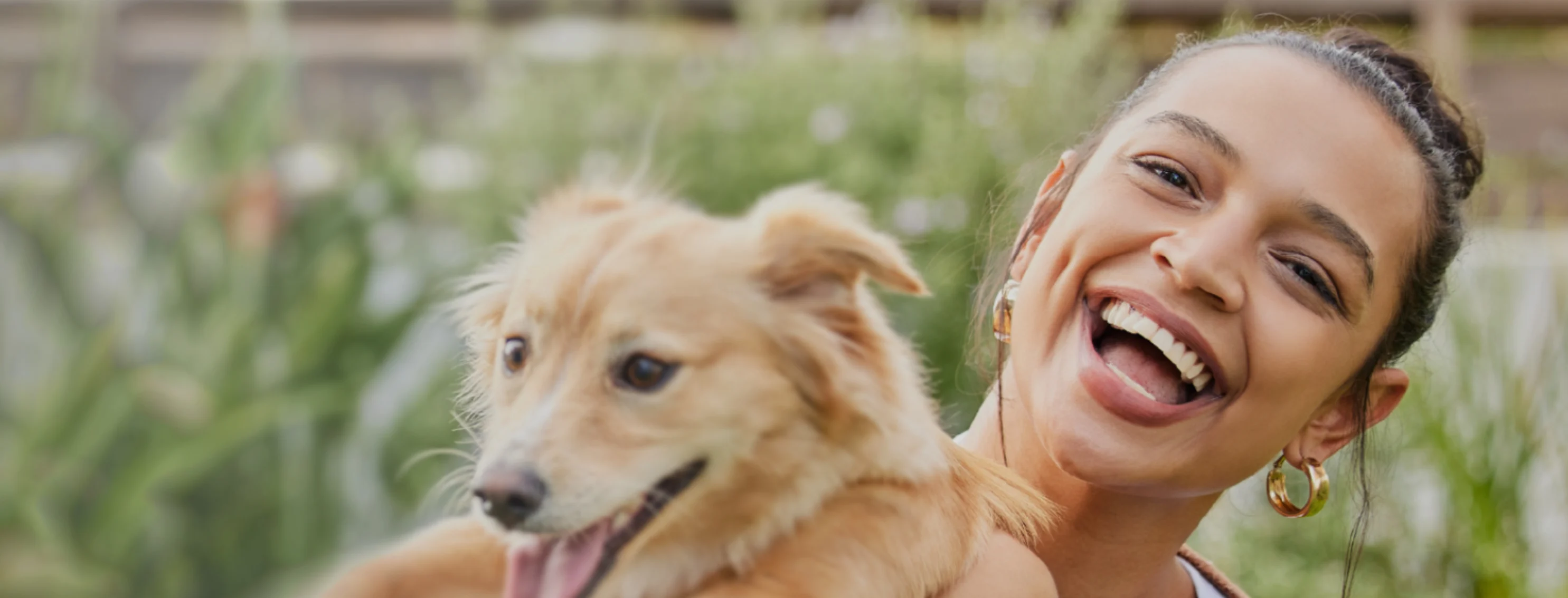 A person holding a small dog in front of a background of greenery