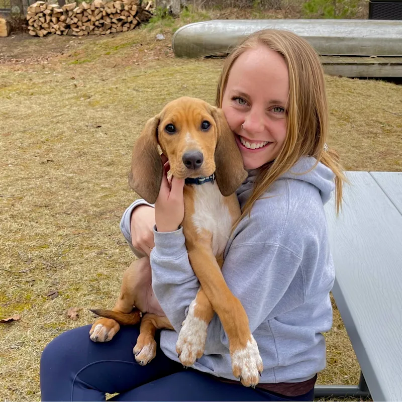 Sydney Snyder sitting outside at a picnic table holding a brown and white dog with long ears Sydney Snyder sitting outside at a picnic table holding a brown and white dog with long ears