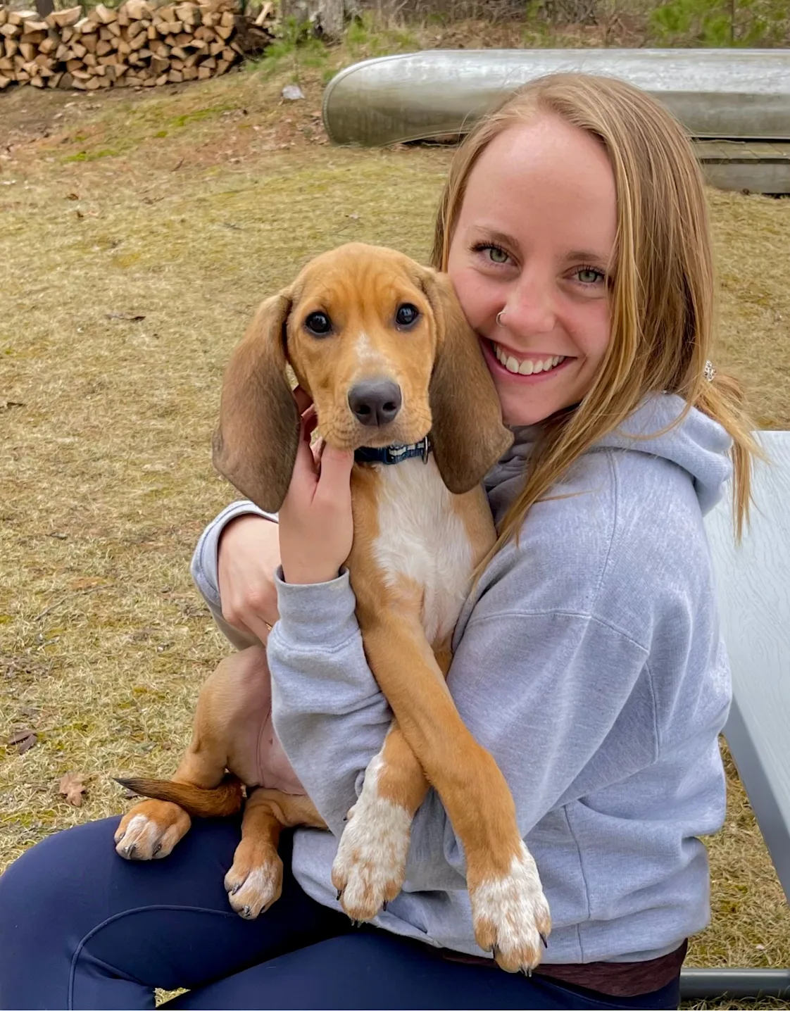 Sydney Snyder sitting outside at a picnic table holding a brown and white dog with long ears Sydney Snyder sitting outside at a picnic table holding a brown and white dog with long ears