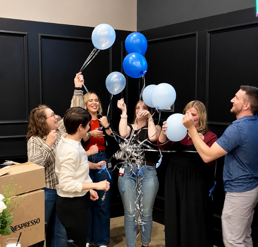 Staff members holding a bundle of blue and white balloons.