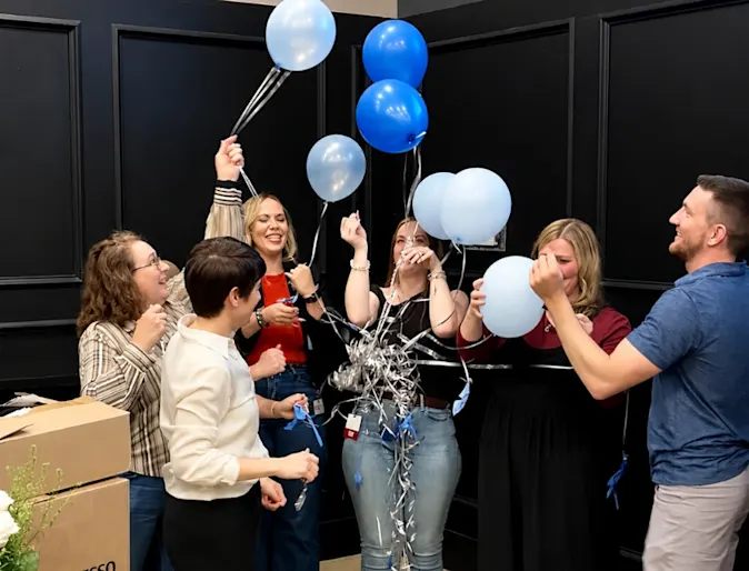 Staff members holding a bundle of blue and white balloons. Staff members holding a bundle of blue and white balloons.