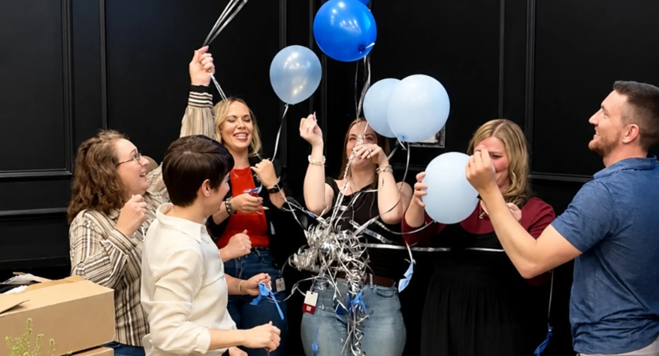 Staff members holding a bundle of blue and white balloons. Staff members holding a bundle of blue and white balloons.