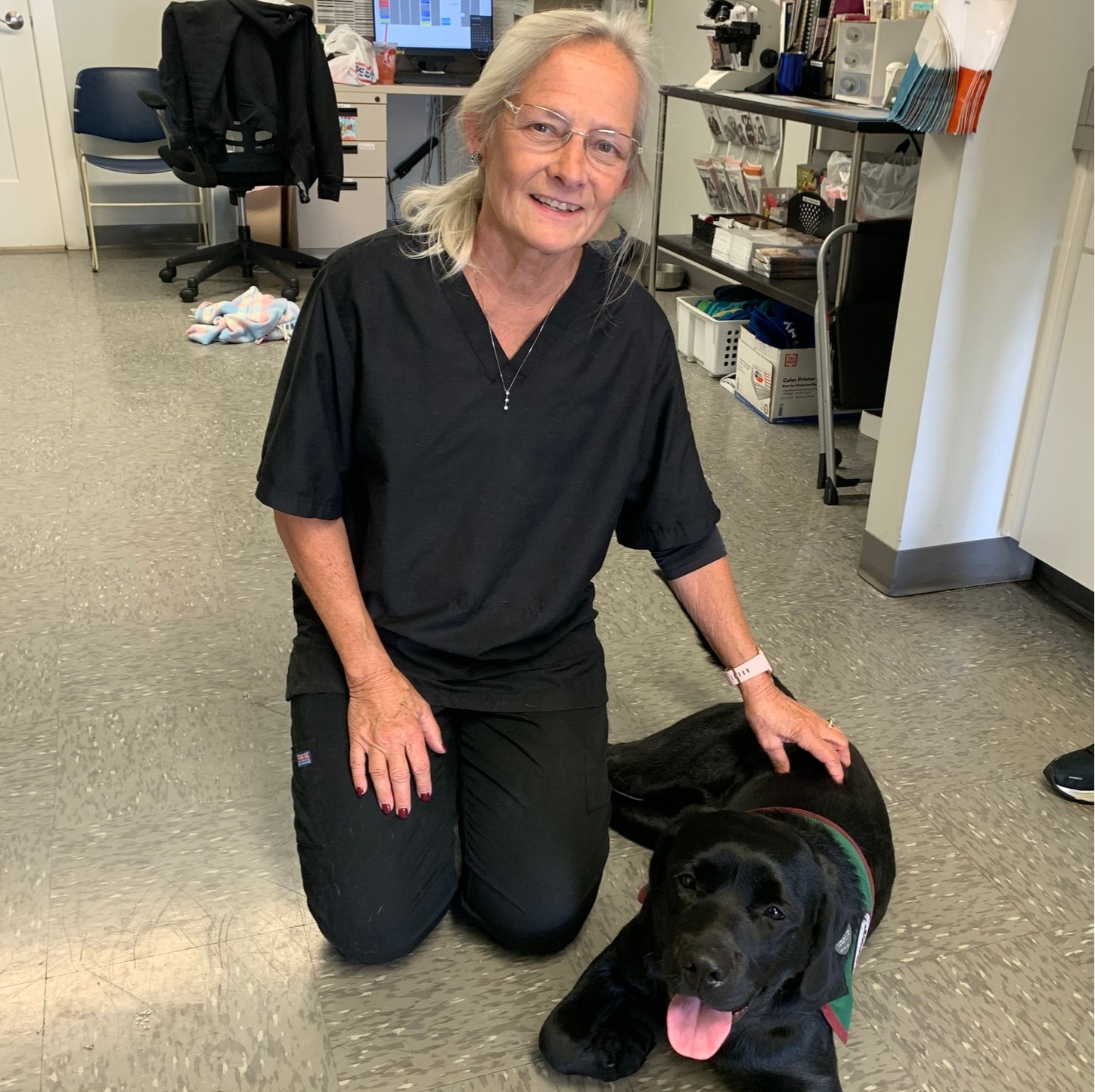 Laurene kneeling down next to a black lab laying on the floor