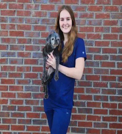 Abbey holding onto a black dog while smiling in front of a brick wall. Abbey holding onto a black dog while smiling in front of a brick wall.