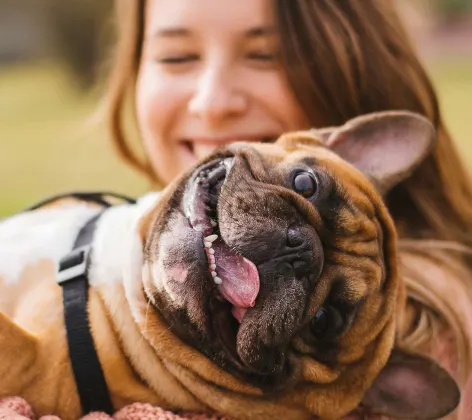 A woman outside smiling and holding a dog in her arms