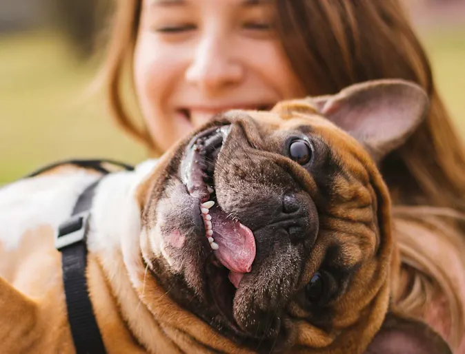 A woman outside smiling and holding a dog in her arms