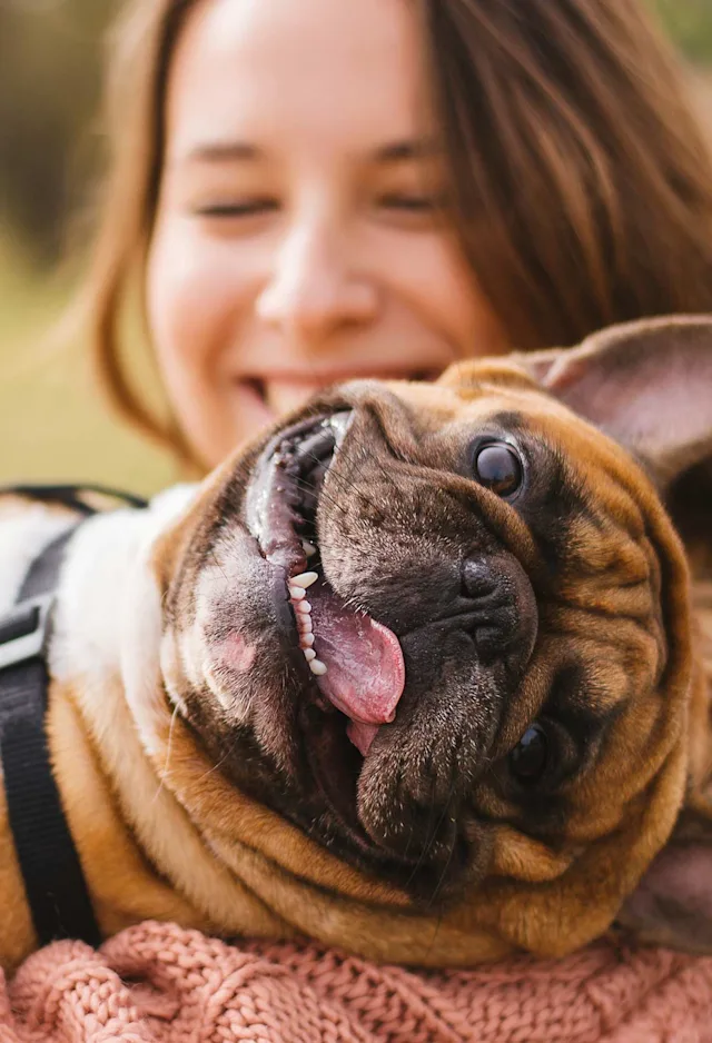 A woman outside smiling and holding a dog in her arms A woman outside smiling and holding a dog in her arms