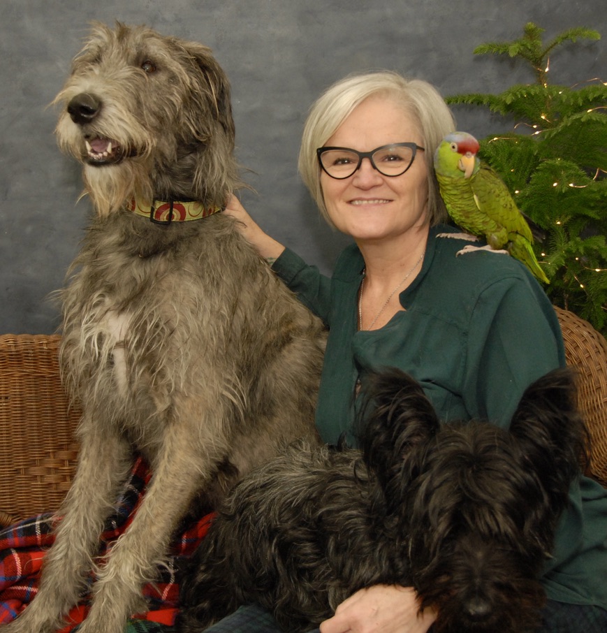 Sandra McBride sitting for a portrait with two dogs and a bird on her shoulder.
