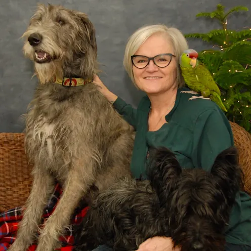 Sandra McBride sitting for a portrait with two dogs and a bird on her shoulder. Sandra McBride sitting for a portrait with two dogs and a bird on her shoulder.