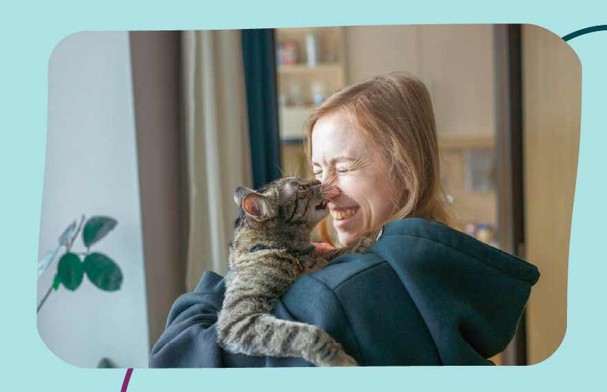 A woman holding a cat in her arms while the cat reaches up and licks the woman's nose.