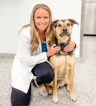 Dr. Jen Brogie smiling kneeling down next to a large brown dog Dr. Jen Brogie smiling kneeling down next to a large brown dog