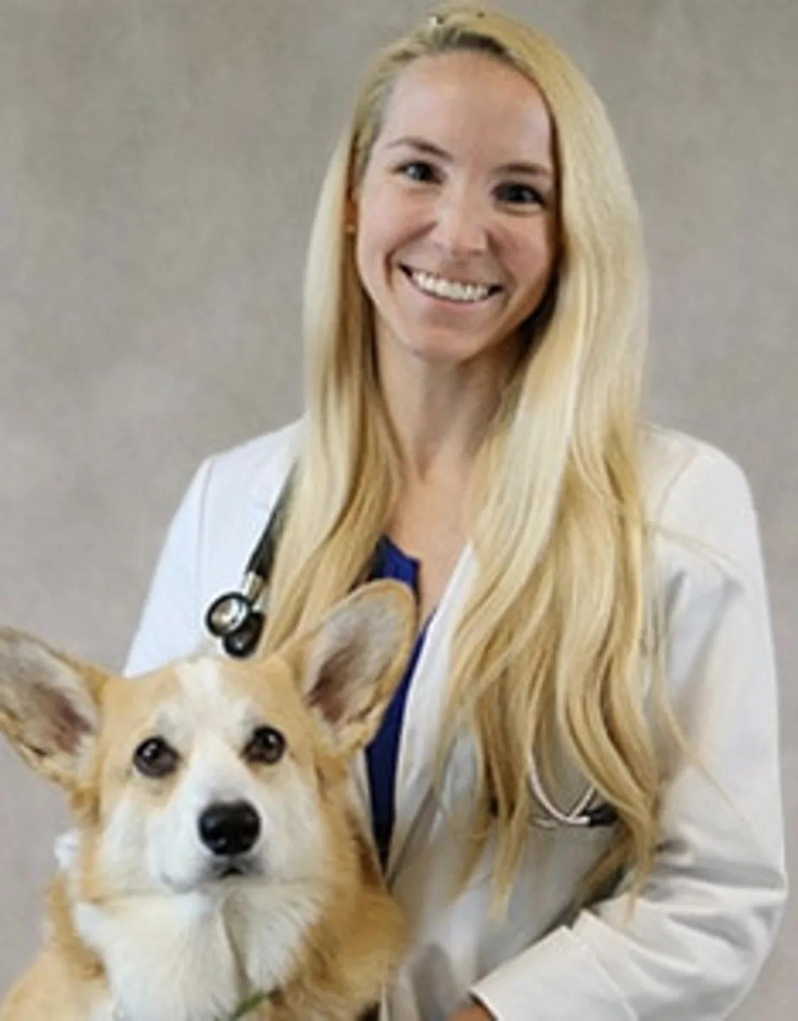 Dr. Alexandra Wood smiling in front of a grey backdrop hugging a Corgi Dr. Alexandra Wood smiling in front of a grey backdrop hugging a Corgi