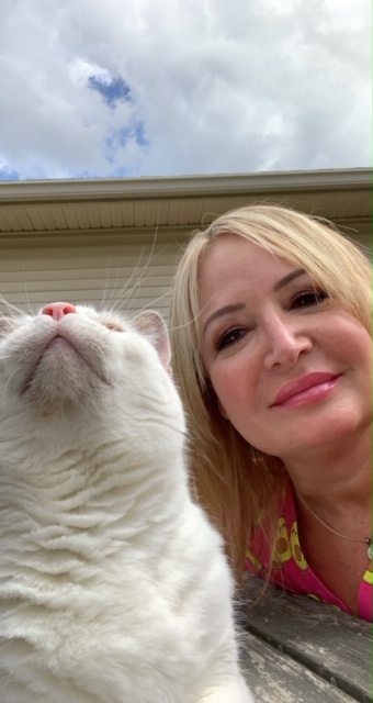 Staff photo from Niles Veterinary Clinic of Linda P. taking a selfie of her and her white cat outside.