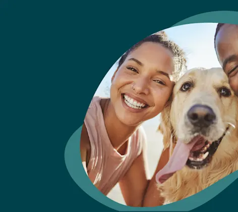 A woman and man smiling outside with their Golden Labrador Retriever between them. A woman and man smiling outside with their Golden Labrador Retriever between them.