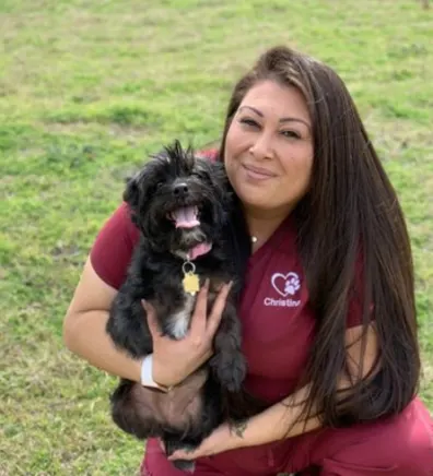 Photo of Christina Balderas holding black dog in the grass