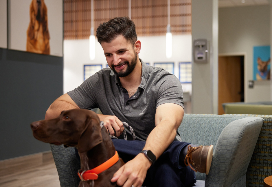 Pet parent sitting in waiting room with brown dog wearing an orange collar