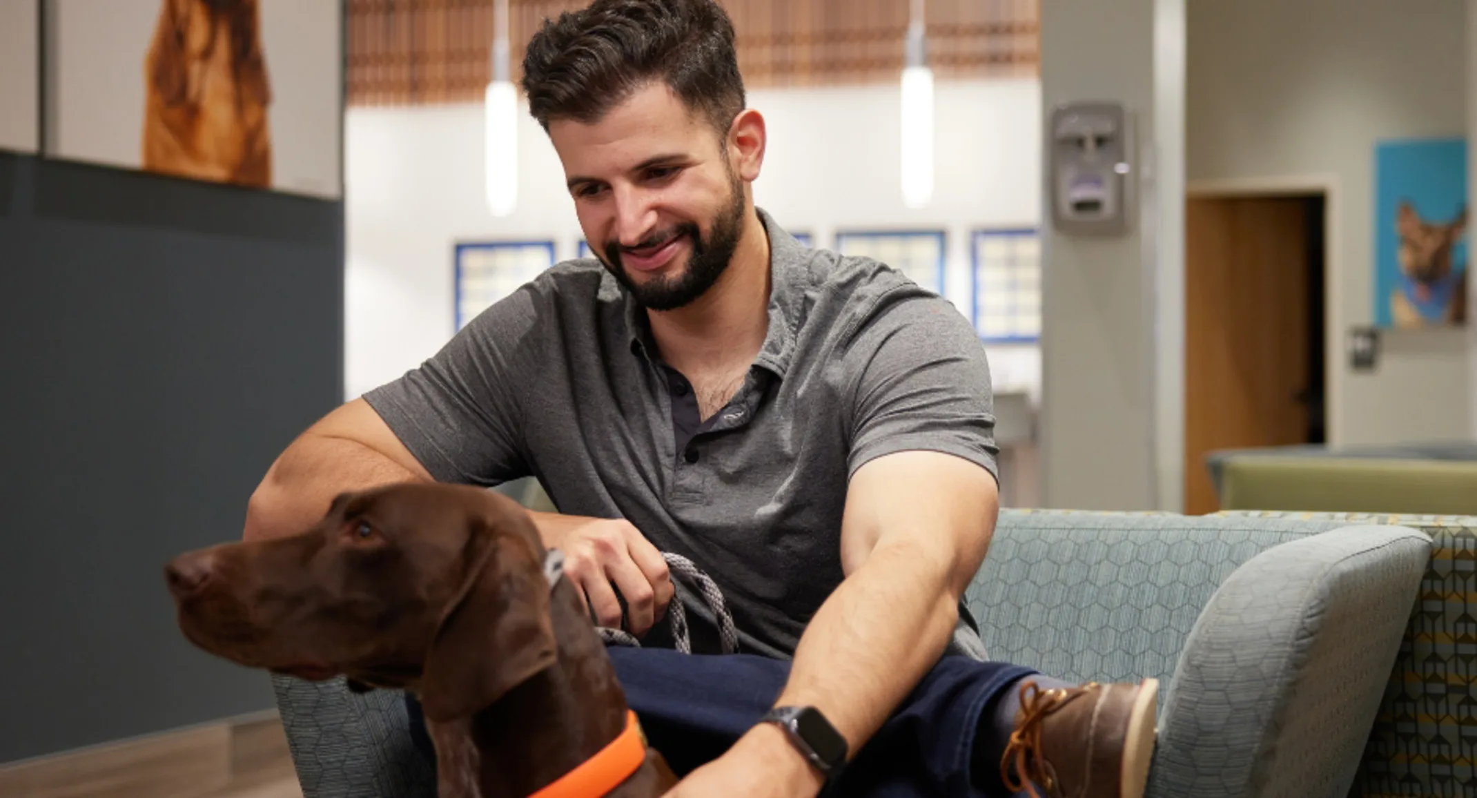 Pet parent sitting in waiting room with brown dog wearing an orange collar Pet parent sitting in waiting room with brown dog wearing an orange collar