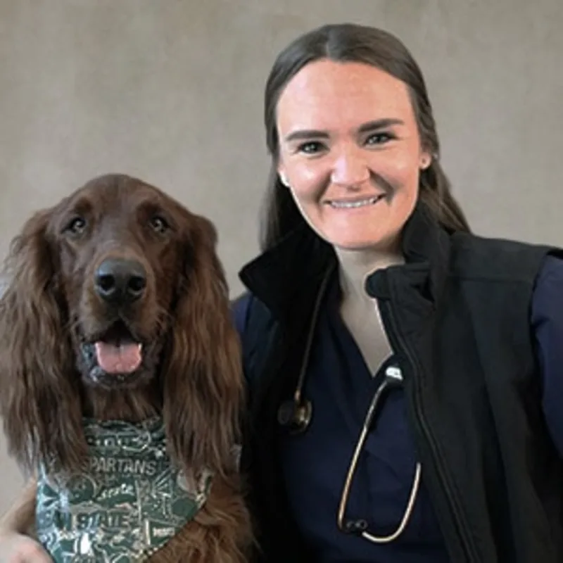 Dr. Katie Haydett Hilton smiling in front of a grey backdrop hugging a large brown dog Dr. Katie Haydett Hilton smiling in front of a grey backdrop hugging a large brown dog