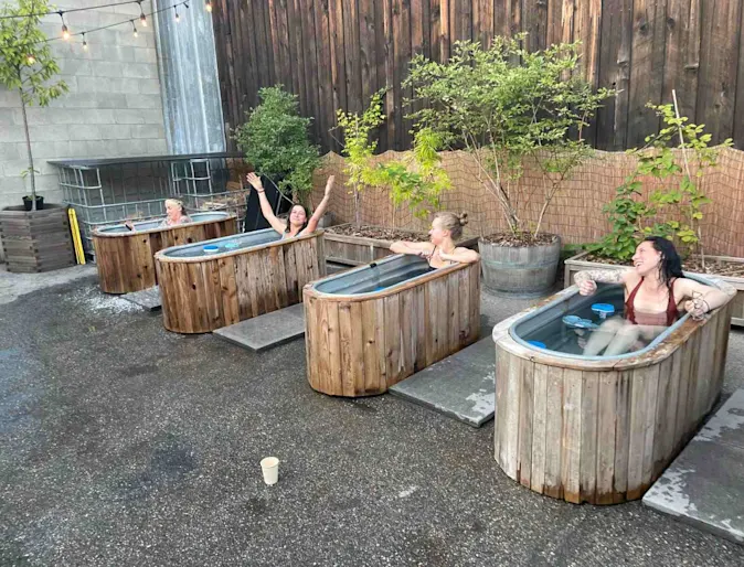 Staff cold plunging in metal tubs outside. Staff cold plunging in metal tubs outside.