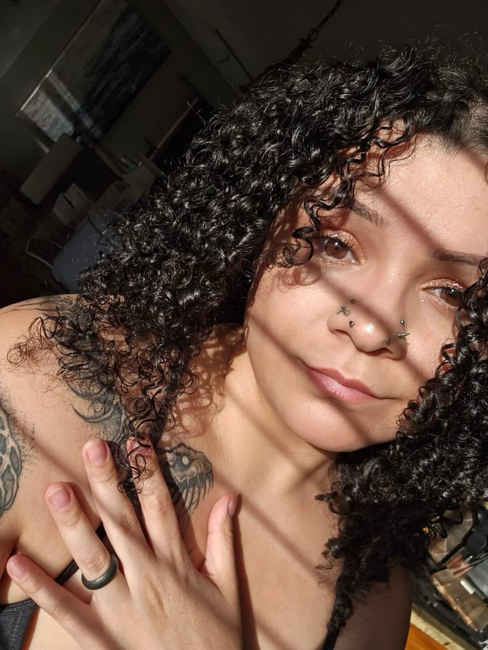 Portrait of a young woman with dark, curly hair, whose sunlight casts lights and shadows on her face.