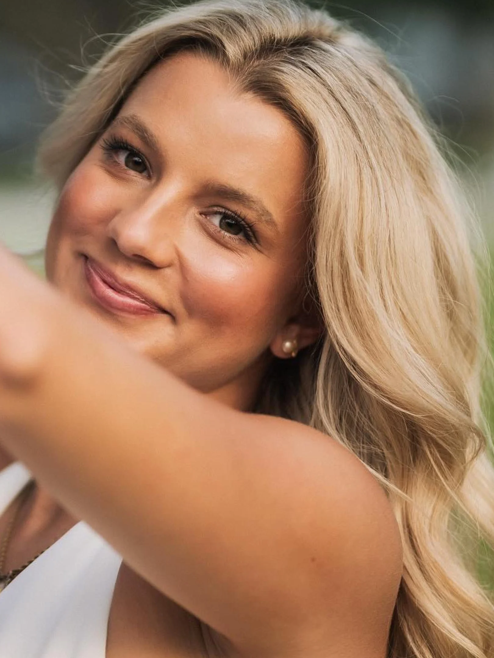 Smiling woman with long, voluminous blonde hair posing outdoors in soft natural light.