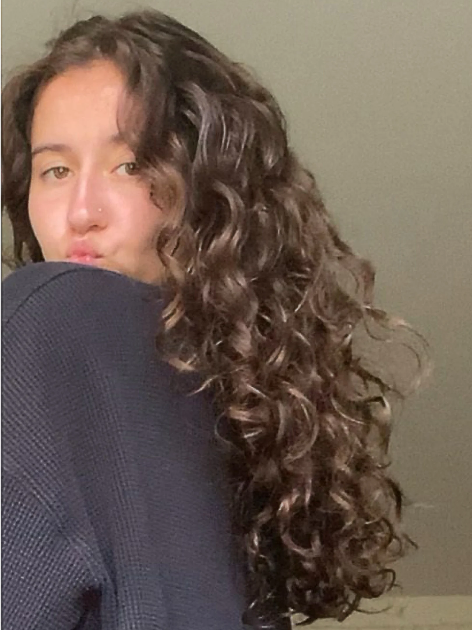 Young woman with dark curly hair looking into the camera and puckering her lips for a kiss.