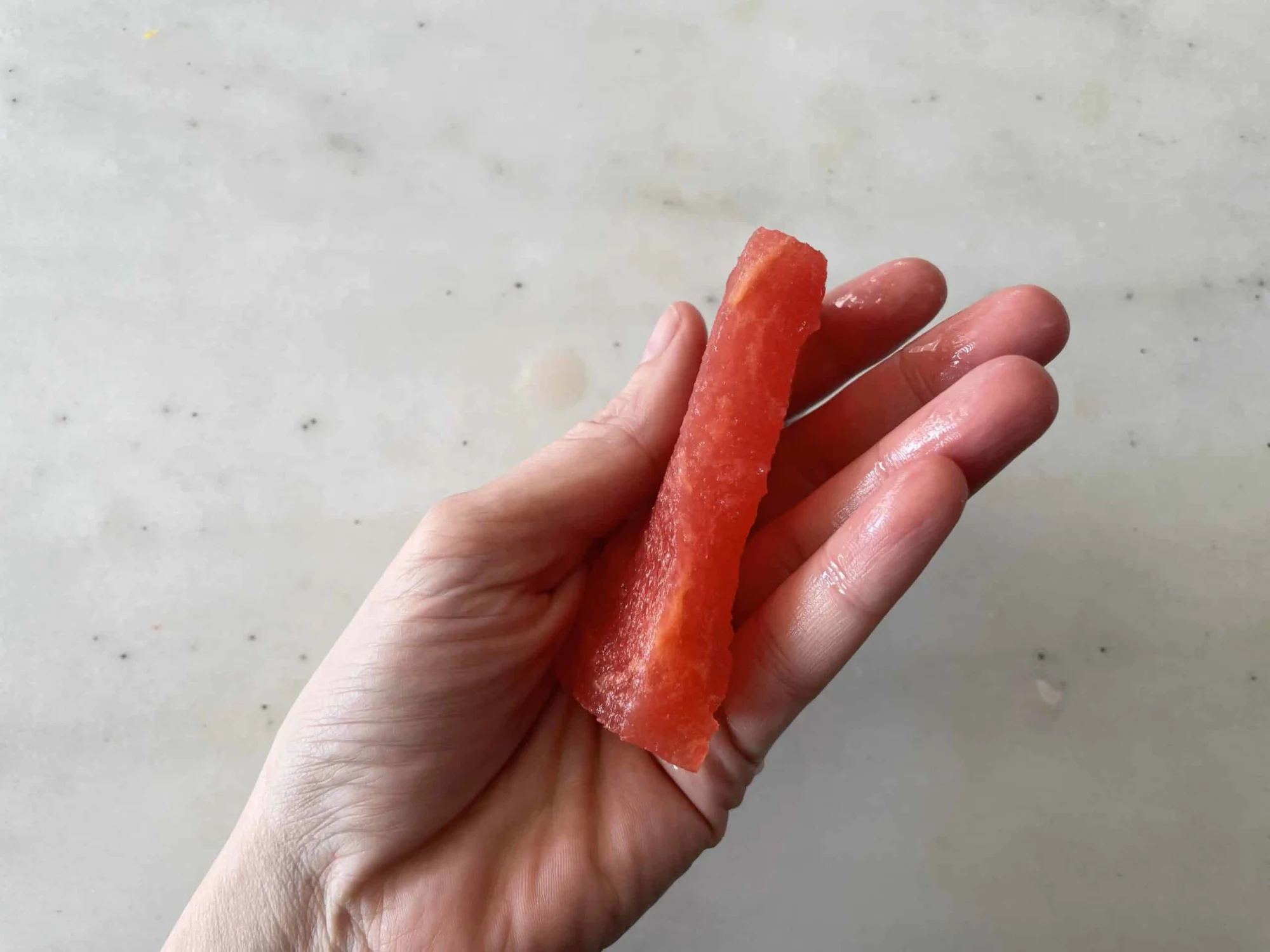 a hand holding a thin rectangular piece of watermelon sideways