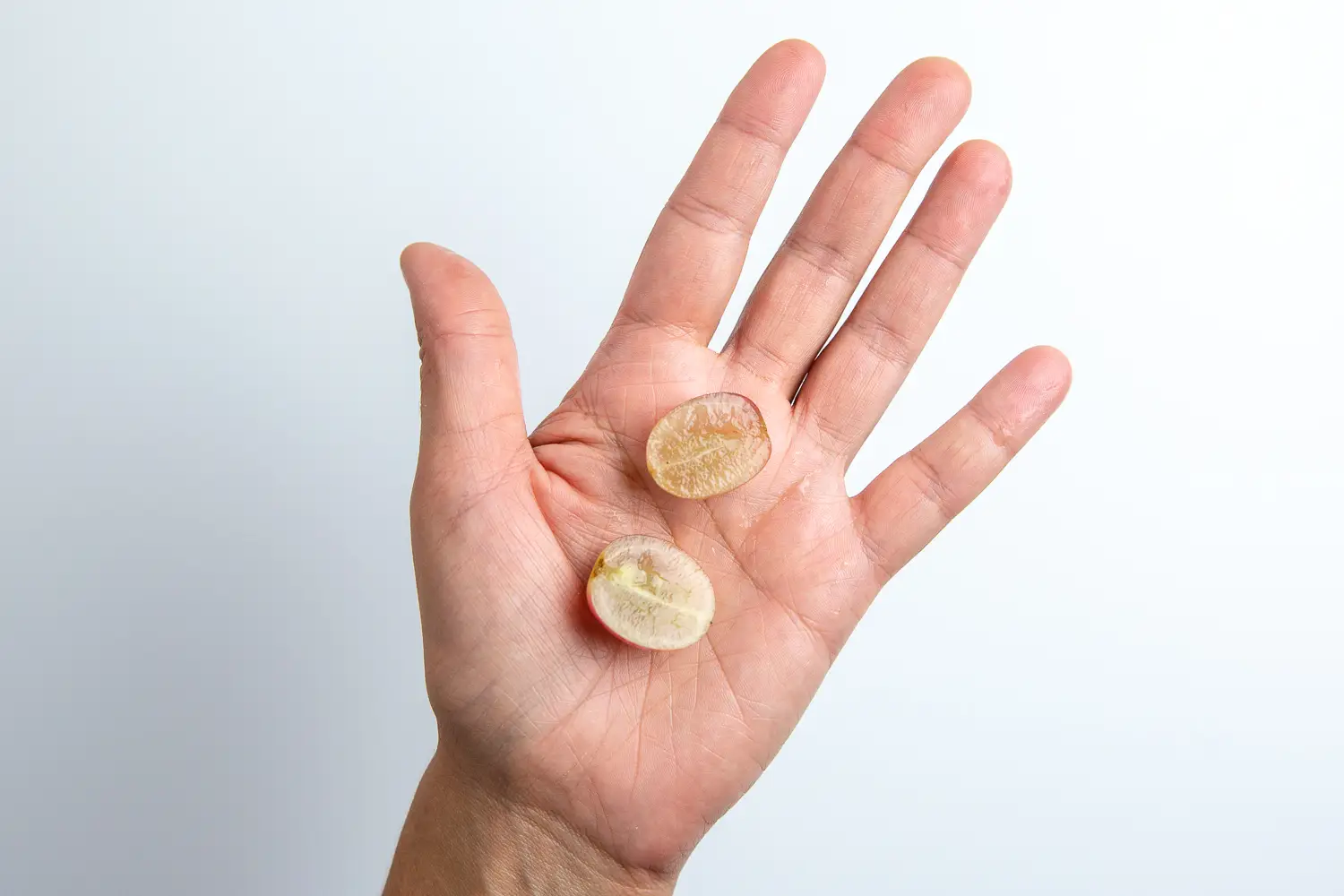 a photograph of a hand holding two pieces of grape cut in half lengthwise