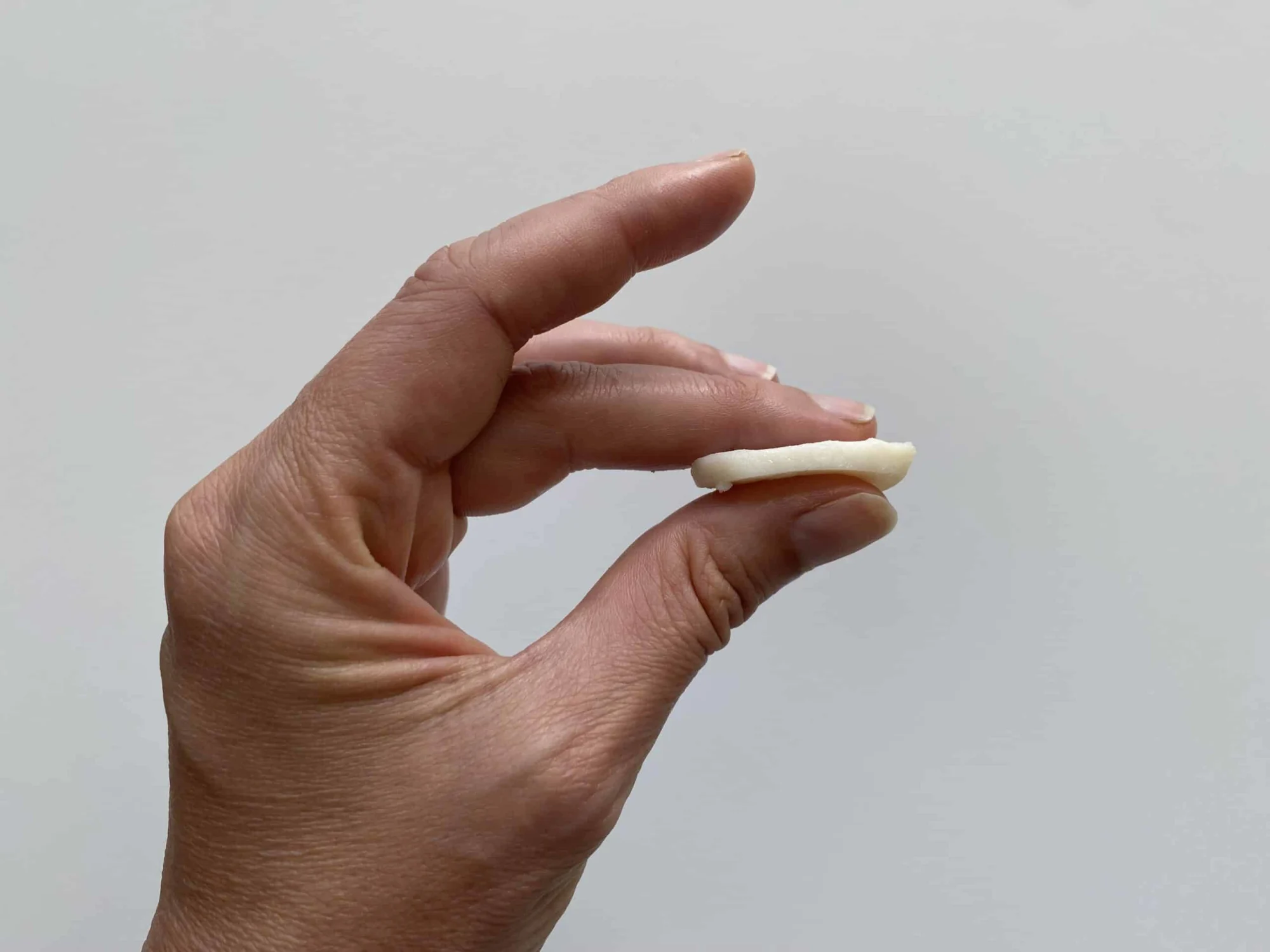 a hand holding a thin slice of cooked scallop in profile so you can see how thin it is
