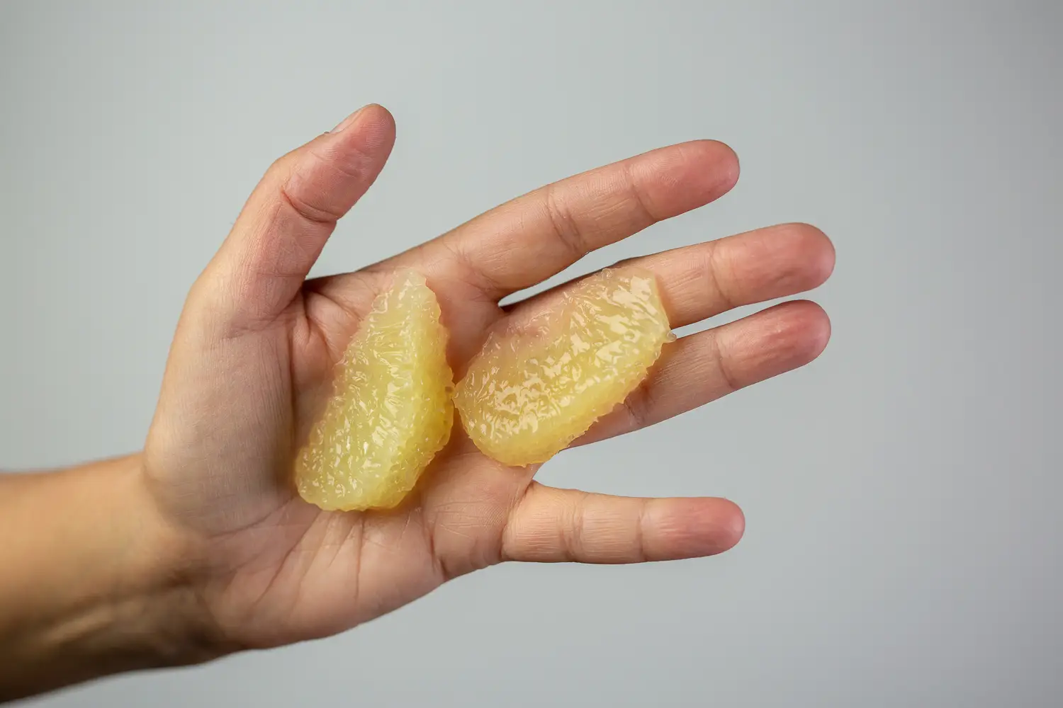 a hand holding two thin yellow slices of oroblanco with membrane and peel removed