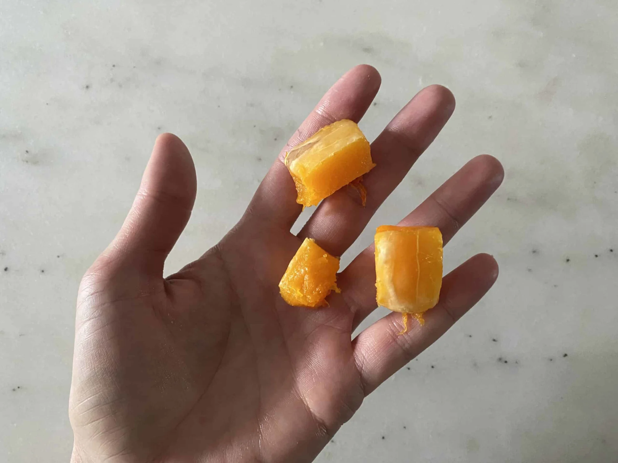 A hand holding three bite-sized pieces of peeled cooked butternut squash for babies 9 months +